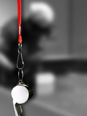 En second plan une photo en noir et blanc dans laquelle on aperçois la silhouette d’un joueur de showdown, au premier plan, un sifflet avec un cordon rouge
